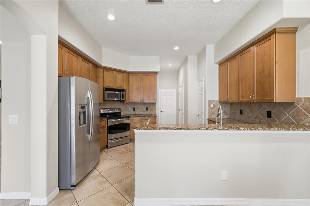 A kitchen with wood cabinets, granite countertops, stainless steel appliances, and tile flooring — 8718 THE ESPLANADE UNIT 14, ORLANDO, FL