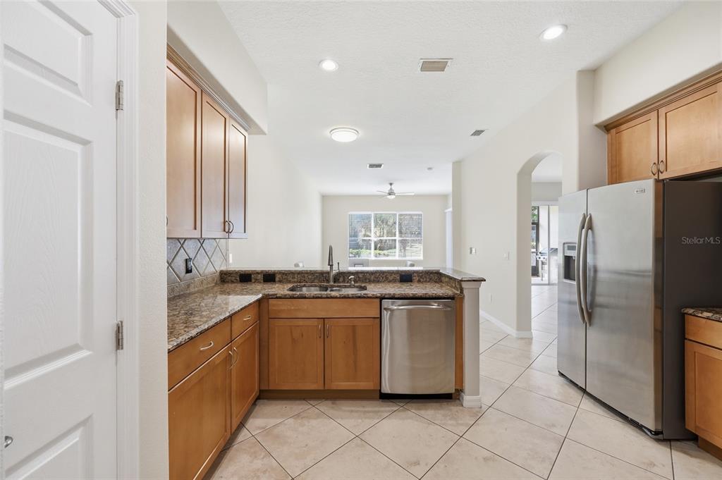 A kitchen features light wood cabinets, granite countertops, stainless steel appliances, and tile flooring — 8718 THE ESPLANADE UNIT 14, ORLANDO, FL