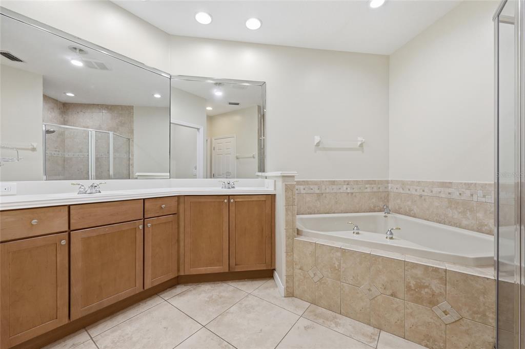 A bathroom features a double vanity with wood cabinets, a tiled soaking tub, and mirrors — 8718 THE ESPLANADE UNIT 14, ORLANDO, FL