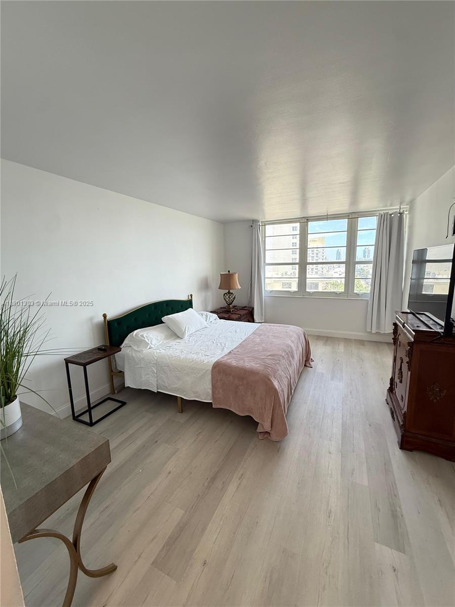 A bedroom features light wood-look flooring, a green headboard, and a large window — 100 Lincoln Rd # 1111, Miami Beach FL 33139, MIAMI BEACH, FL