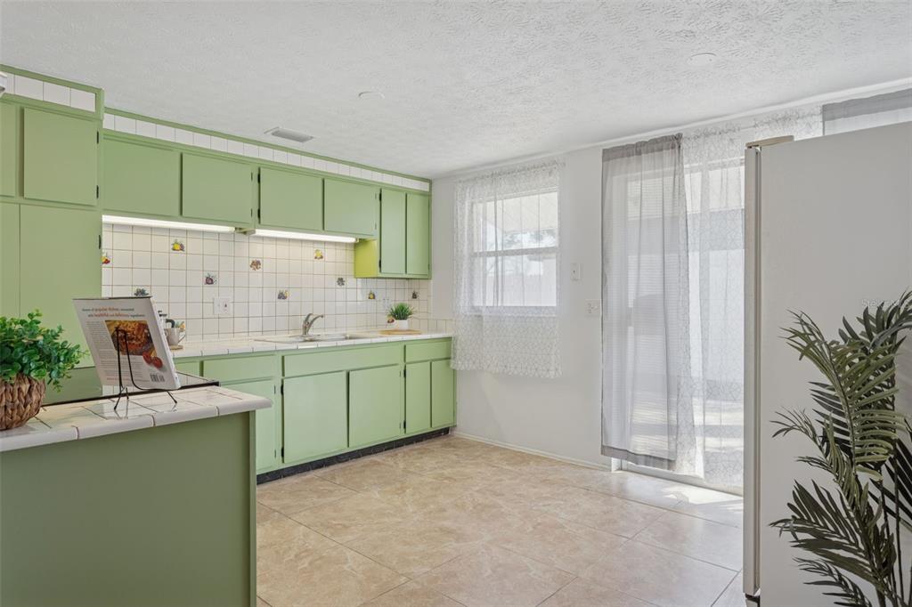 A kitchen features light green cabinets, white tiled walls with decorative accents, and tile flooring — 8105 ALPINE AVENUE, TAMPA, FL