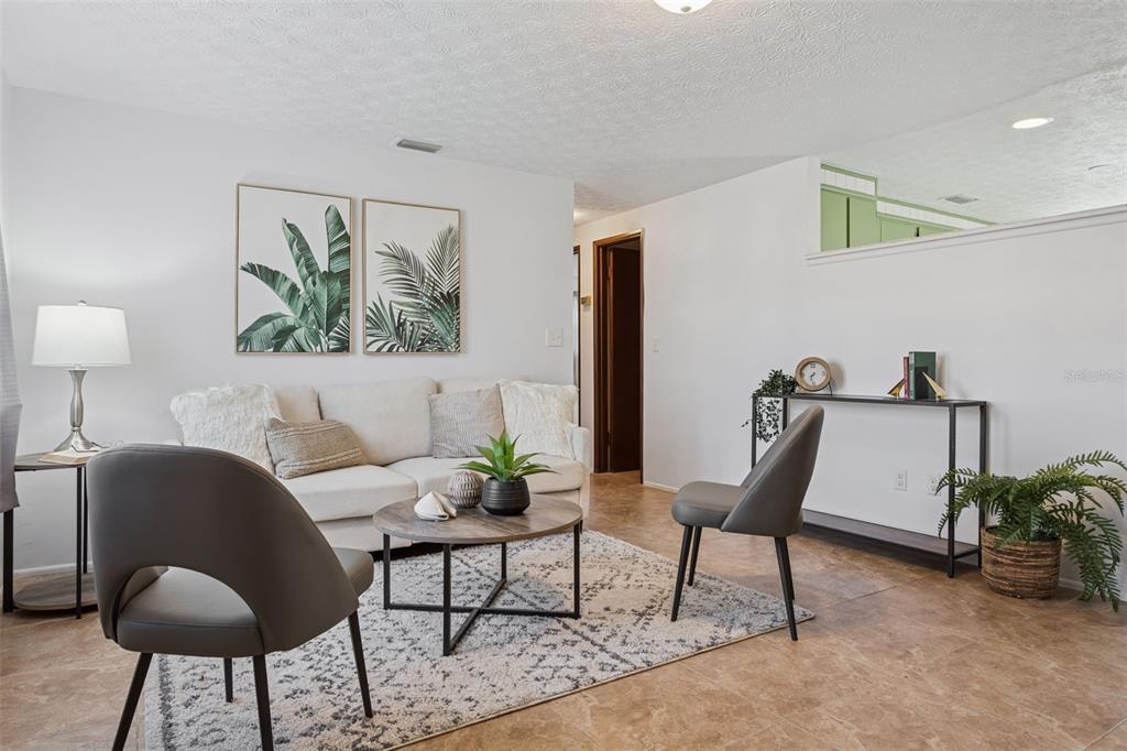 A living room features a gray sofa, patterned armchairs, a glass coffee table, and tile flooring — 8105 ALPINE AVENUE, TAMPA, FL