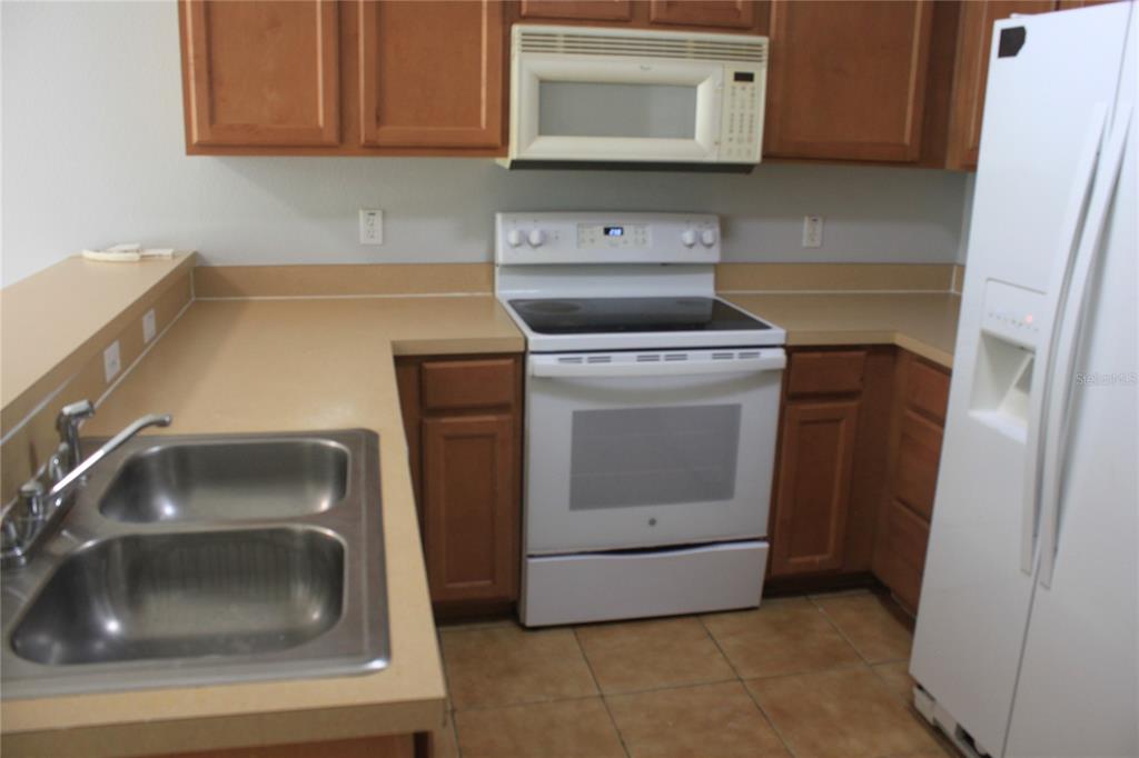A kitchen features wood cabinets, white appliances, a double sink, and tan countertops — 669 CRESTING OAK CIRCLE UNIT 30, ORLANDO, FL