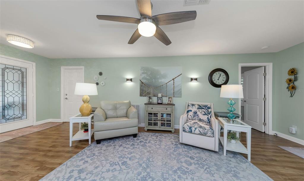 A living room features two armchairs, a central cabinet, and a ceiling fan on light-green walls — 1308 GILLESPIE DRIVE, PALM HARBOR, FL