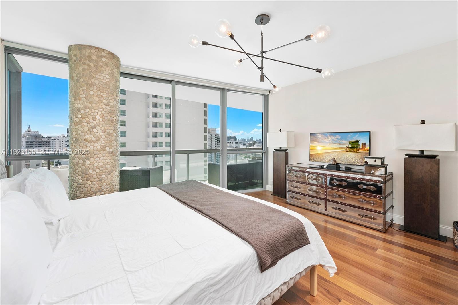 A bedroom features a pebble-covered column, a modern chandelier, and floor-to-ceiling windows with city views — 101 20th St # 1706, Miami Beach FL 33139, MIAMI BEACH, FL