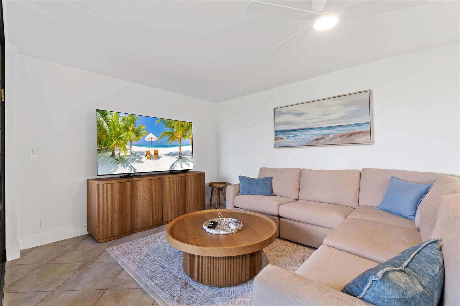 A living room features a beige sectional sofa, a round wooden coffee table, and television — 2455 Lindell Boulevard # 3103, Delray Beach FL 33444, DELRAY BEACH, FL