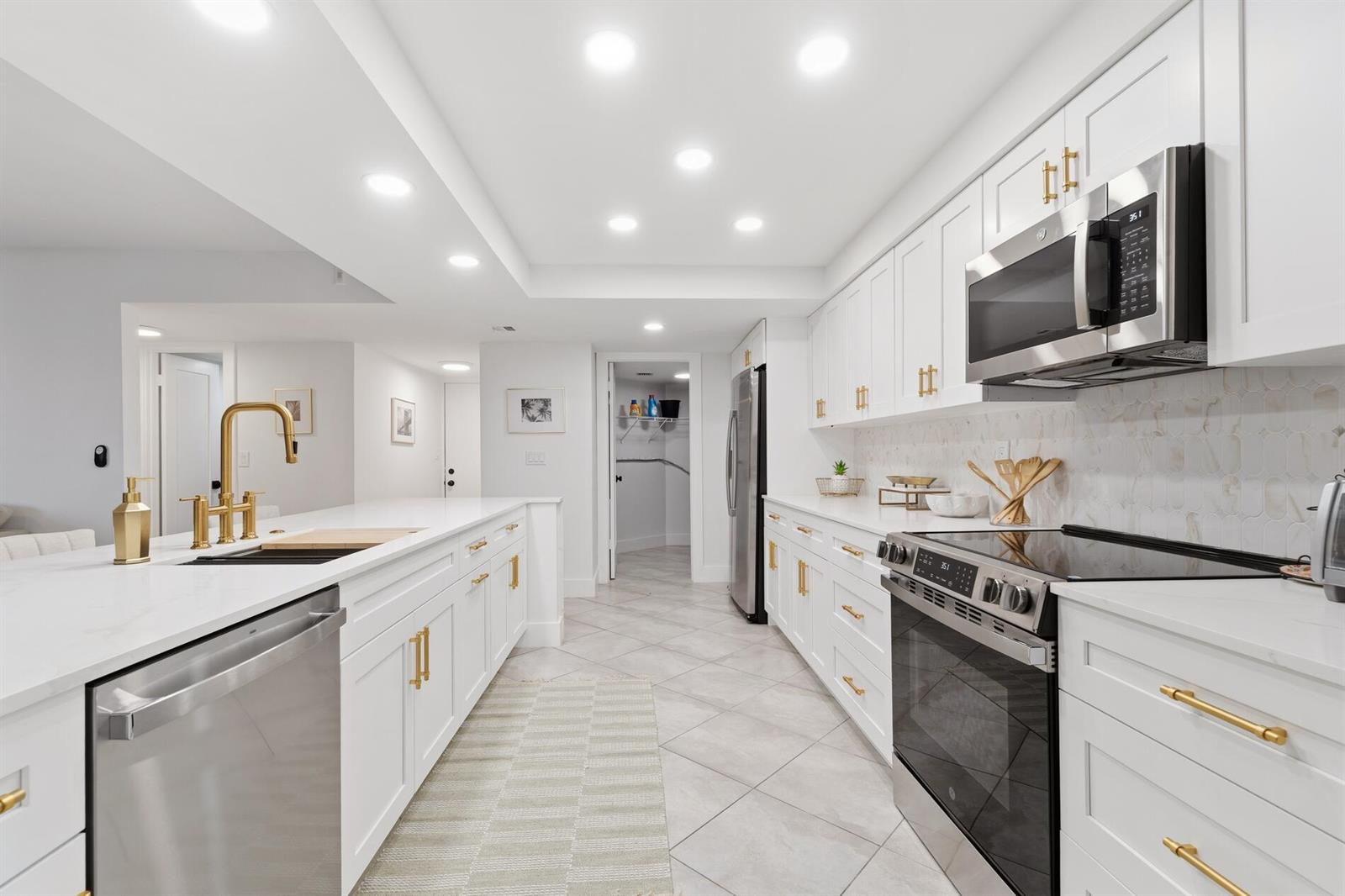 A modern white kitchen features gold hardware, stainless steel appliances, and light-colored tile flooring — 2455 Lindell Boulevard # 3103, Delray Beach FL 33444, DELRAY BEACH, FL
