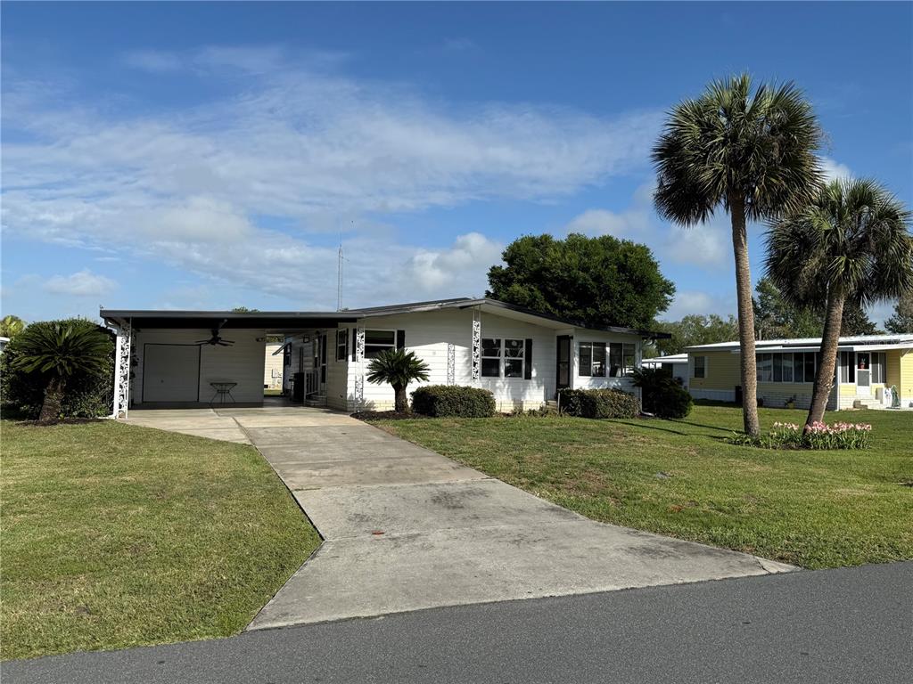 A white single-story house with a carport and palm trees sits on a grassy lot — 11 N BOBWHITE ROAD, WILDWOOD, FL