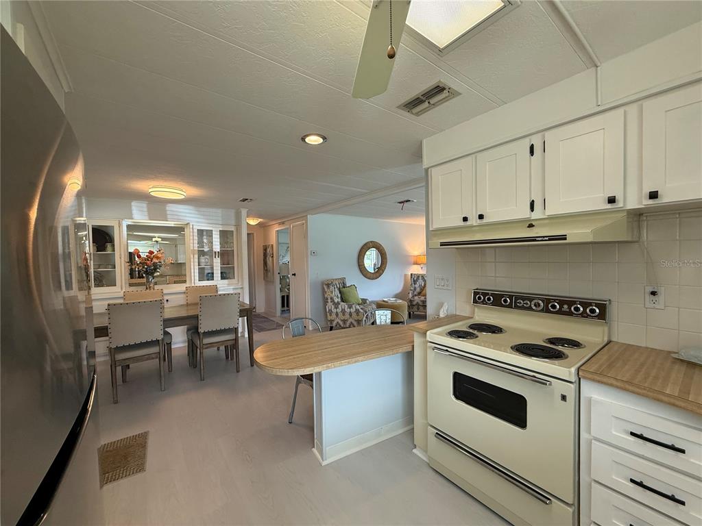 A kitchen with white cabinets and a stove overlooks a dining area and living room — 11 N BOBWHITE ROAD, WILDWOOD, FL