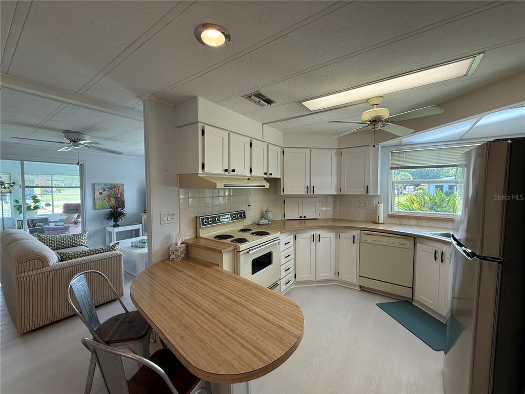 A kitchen with white cabinets, a wood-look peninsula, and a dining area in the background — 11 N BOBWHITE ROAD, WILDWOOD, FL