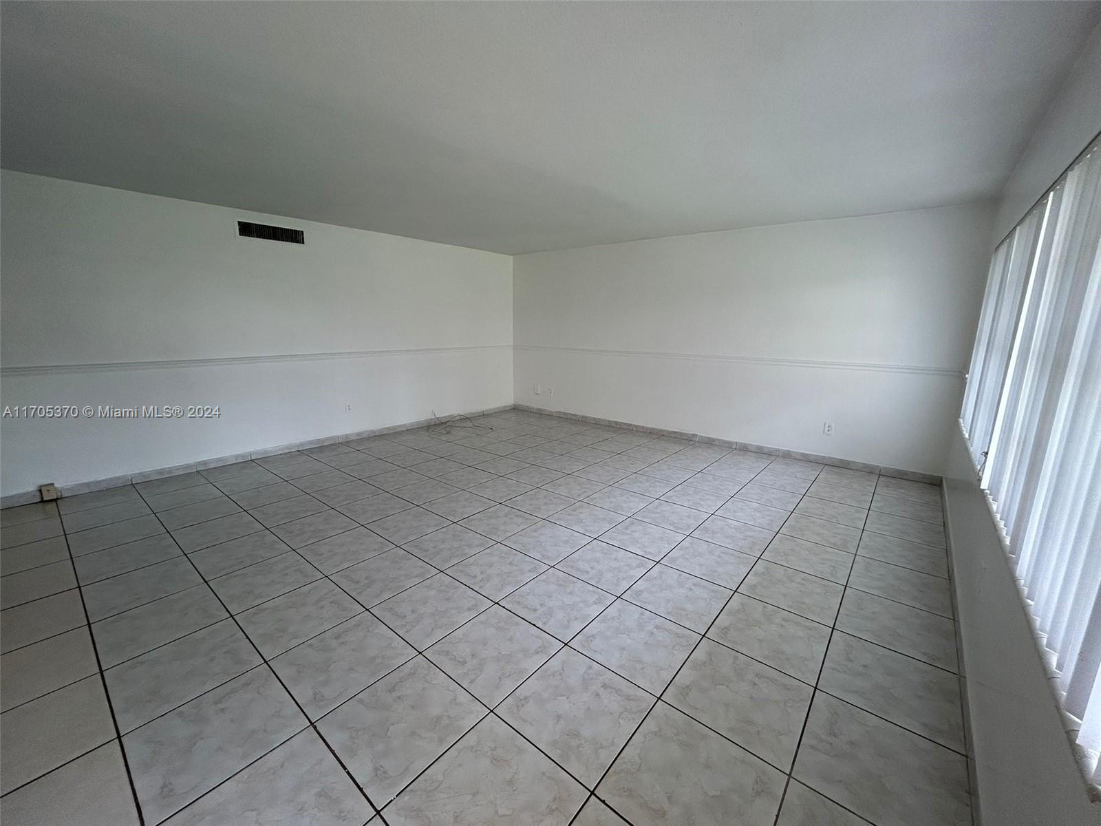 An empty room features white walls, a chair rail, and light-colored square floor tiles — 11855 NE 19th Dr # 8, North Miami FL 33181, NORTH MIAMI, FL