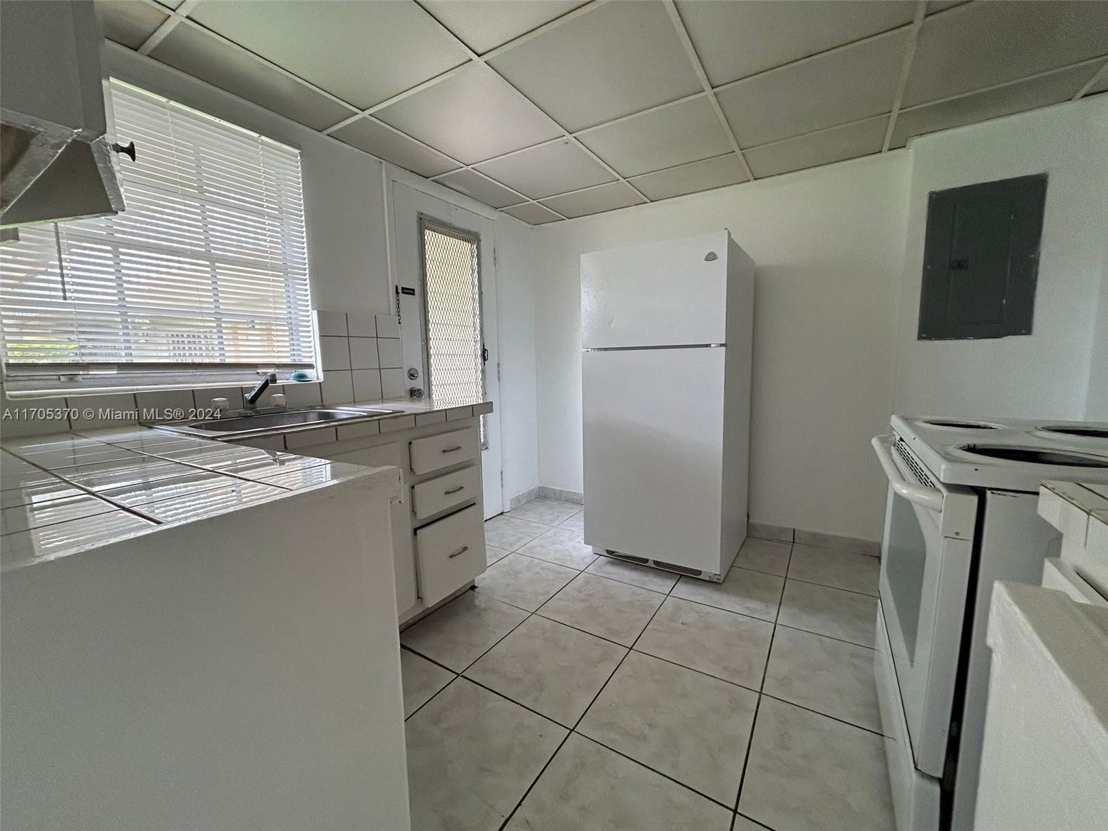 A kitchen features white appliances, tiled countertops, a drop ceiling, and light-colored floor tiles — 11855 NE 19th Dr # 8, North Miami FL 33181, NORTH MIAMI, FL