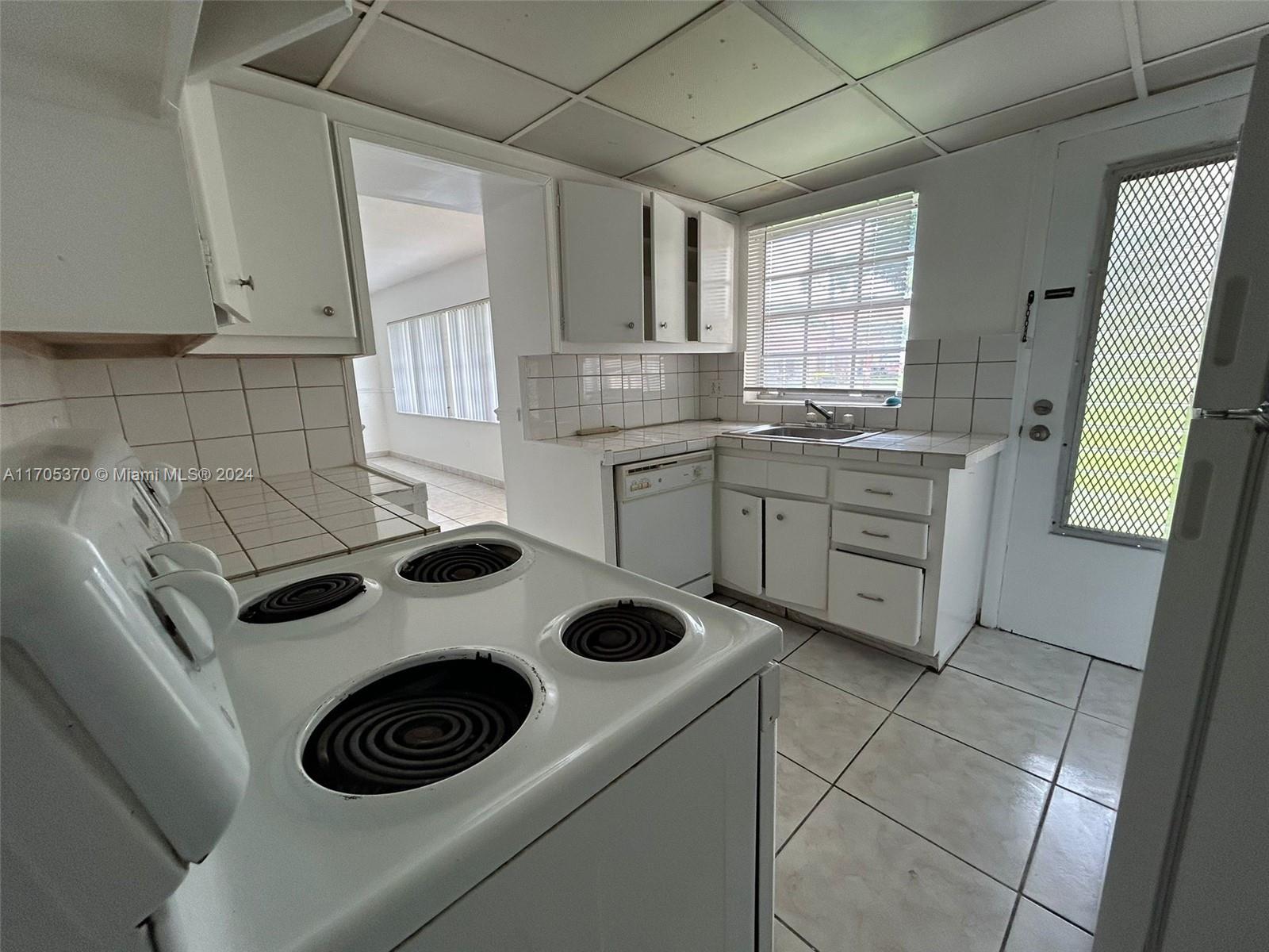 A white kitchen features tile countertops, a stove, a dishwasher, and a tiled floor — 11855 NE 19th Dr # 8, North Miami FL 33181, NORTH MIAMI, FL