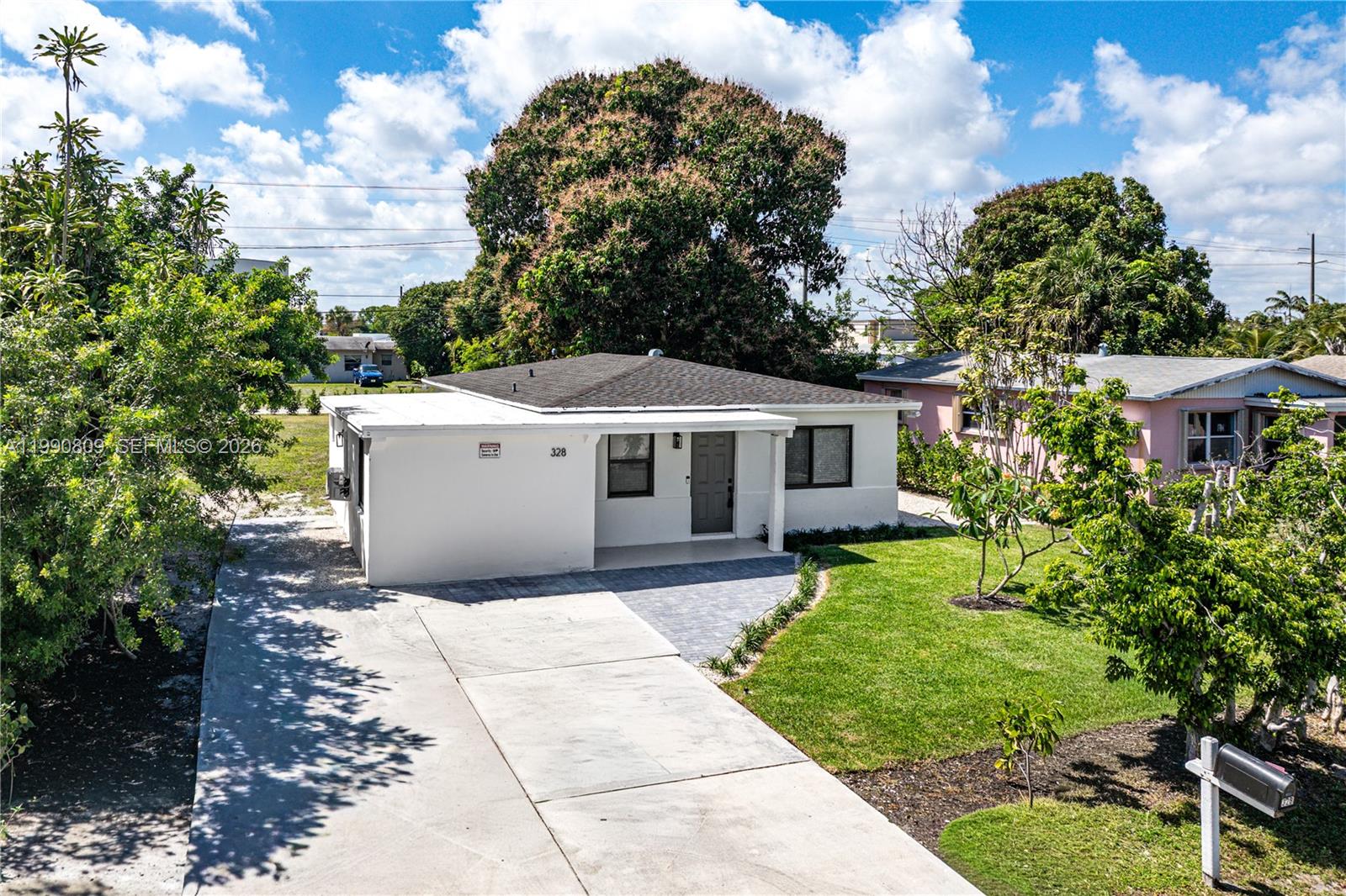 An exterior view of a white, single-story house with a concrete driveway and front lawn — 328 SW 11th Ave, Delray Beach FL 33444, DELRAY BEACH, FL