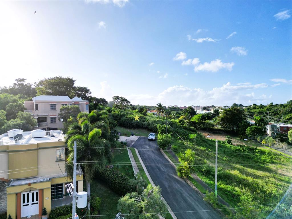 An elevated view shows a paved road, a white car, and houses surrounded by greenery — HACIENDAS DE CAMUY LOTE 9, CAMUY, PR