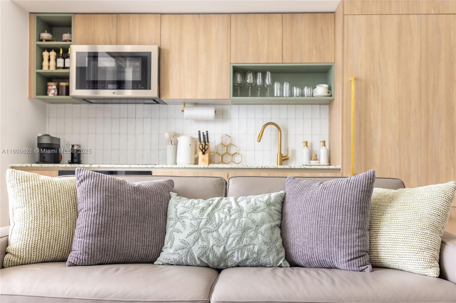 A modern kitchen with light wood cabinets and a gray sofa in the foreground — 159 NE 6th St # 3001, Miami FL 33132, MIAMI, FL