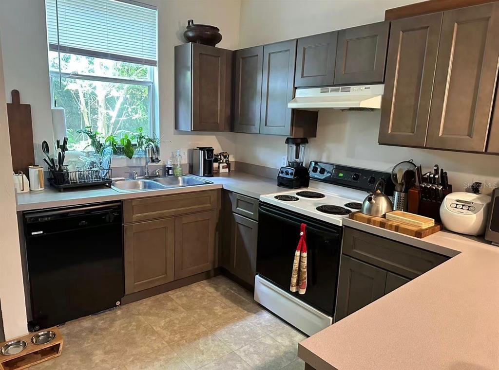 A kitchen features dark wood cabinets, laminate countertops, a black dishwasher, and a white stove — 3940 SW 20TH AVENUE UNIT 1107, GAINESVILLE, FL