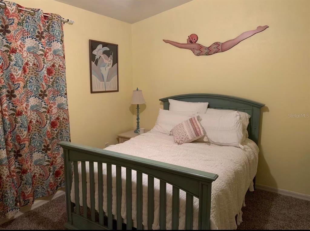 A bedroom features a green bed frame, yellow walls, patterned curtains, and a swimmer wall decoration — 3940 SW 20TH AVENUE UNIT 1107, GAINESVILLE, FL