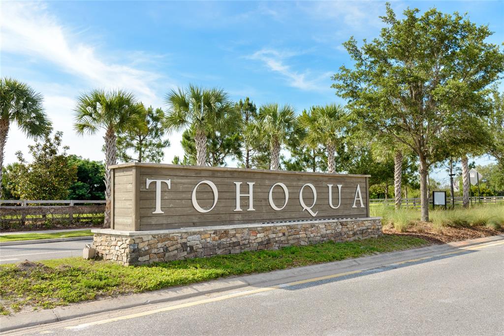 A wooden sign with the name Tohoqua sits on a stone base near palm trees — 2579 RELAXING LANE, KISSIMMEE, FL