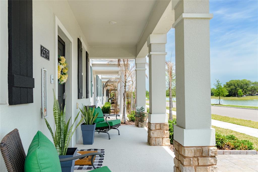 A covered front porch features stone-based columns, green patio furniture, and a view of water — 2579 RELAXING LANE, KISSIMMEE, FL