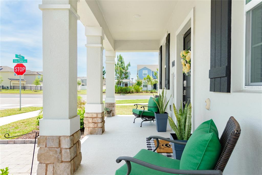 A covered front porch features stone-based columns, green patio chairs, and potted snake plants — 2579 RELAXING LANE, KISSIMMEE, FL