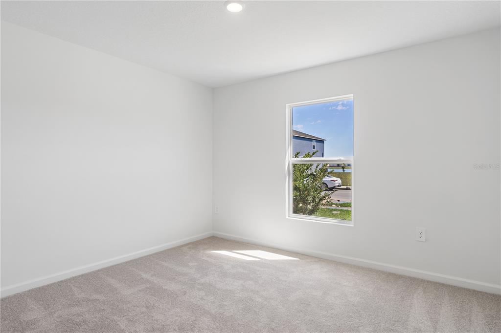 An empty bedroom features white walls, beige carpeting, and a single window overlooking a street — 4814 YELLOW ELDER WAY, KISSIMMEE, FL