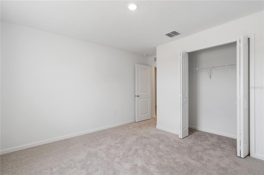 A bedroom features white walls, beige carpeting, a closet with folding doors, and an open door — 4814 YELLOW ELDER WAY, KISSIMMEE, FL