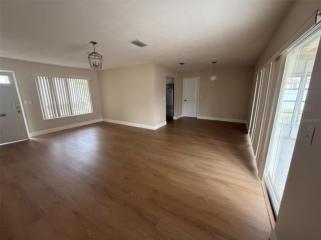 An open-concept living area features light wood-look flooring, neutral walls, and a sliding glass door — 6568 TREEHAVEN DRIVE, SPRING HILL, FL