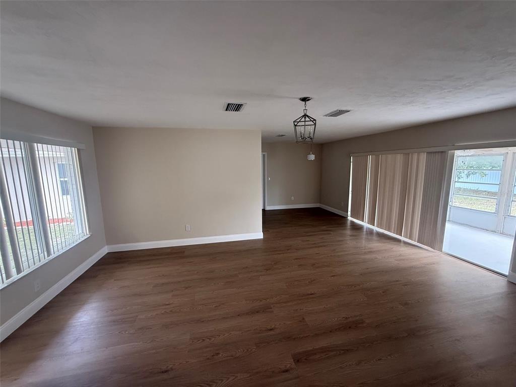 An empty living area features dark wood-look flooring, beige walls, and large sliding glass doors — 6568 TREEHAVEN DRIVE, SPRING HILL, FL