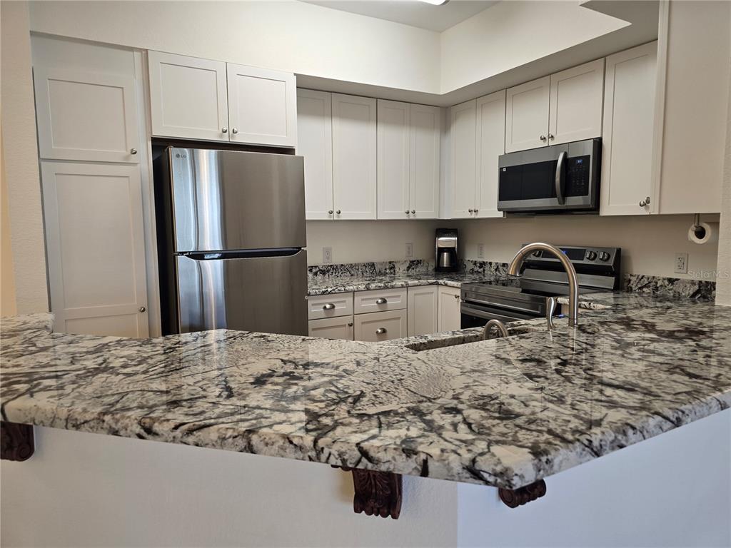 A kitchen features white cabinets, stainless steel appliances, and a large granite countertop island — 4170 CENTRAL SARASOTA PARKWAY UNIT 412, SARASOTA, FL