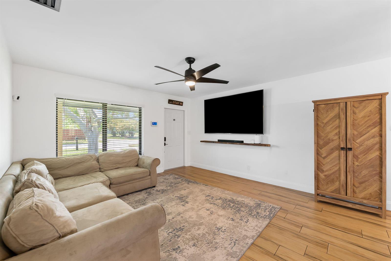 A living room features a beige sectional sofa, a wall-mounted television, and wood-look flooring — 1032 SW 1st Terrace, Pompano Beach FL 33060, POMPANO BEACH, FL