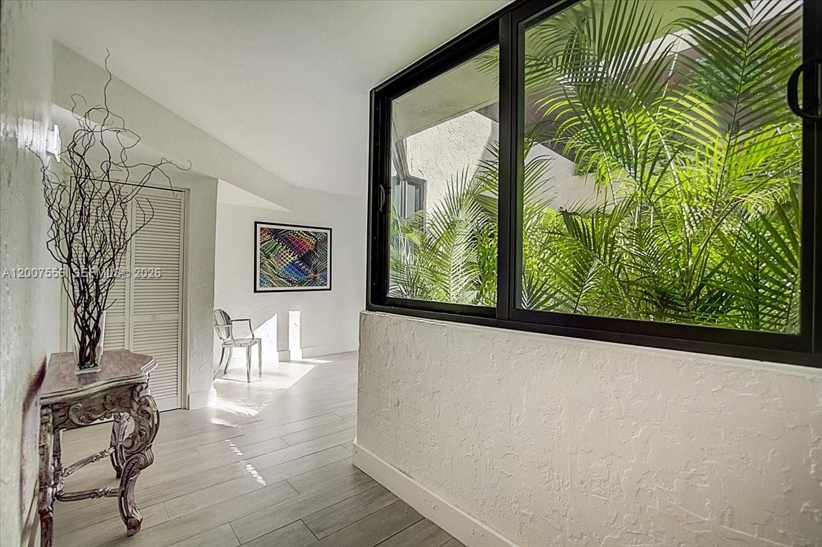 A bright hallway features white walls, light wood-look flooring, and a large window with greenery — 101 E Crandon Blvd # 276, Key Biscayne FL 33149, KEY BISCAYNE, FL