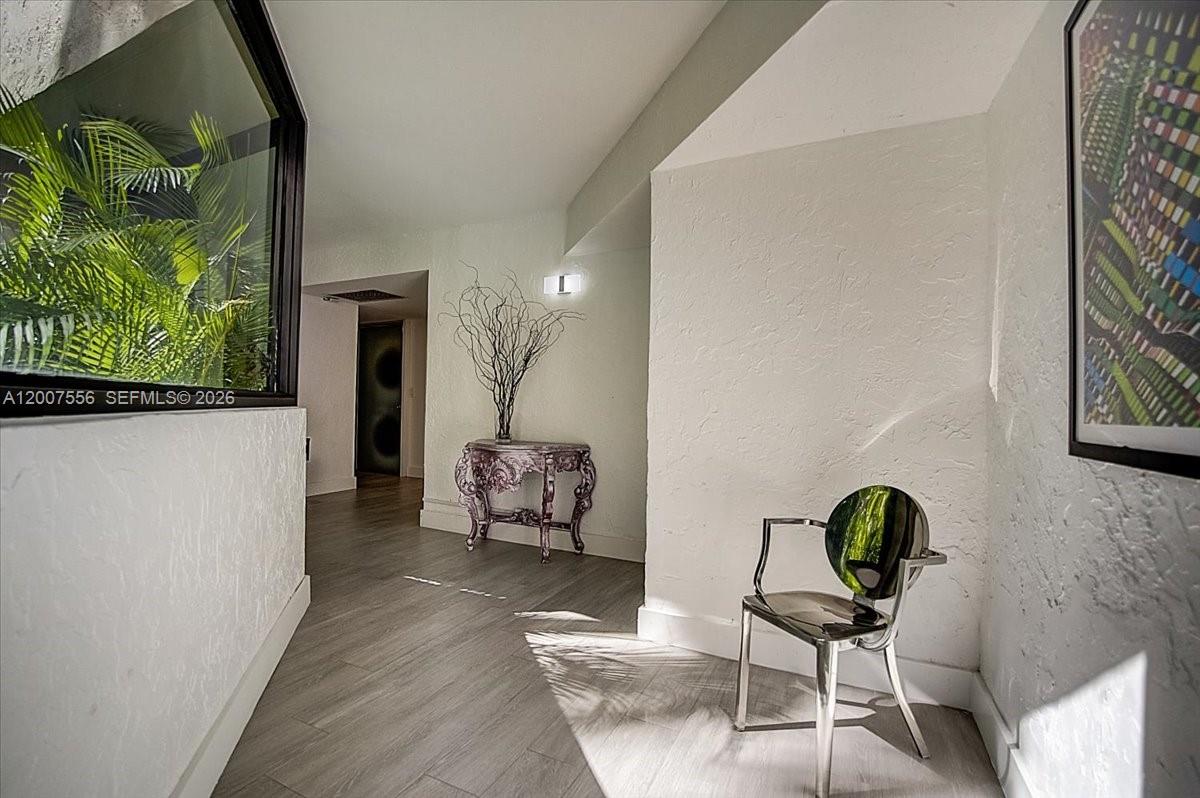 A hallway features light wood-look flooring, white textured walls, a decorative console table, and a modern chair — 101 E Crandon Blvd # 276, Key Biscayne FL 33149, KEY BISCAYNE, FL