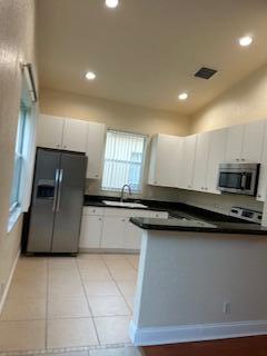 A kitchen with white cabinets, stainless steel appliances, dark countertops, and light tile flooring — 6211 Arlington Way, Fort Pierce FL 34951, FORT PIERCE, FL