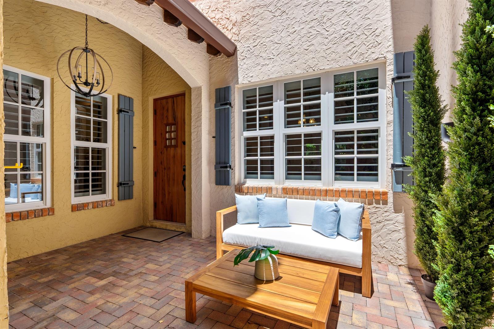 A patio with a wooden bench, coffee table, and a wooden door under an archway — 1027 Coralina Lane, Delray Beach FL 33483, DELRAY BEACH, FL