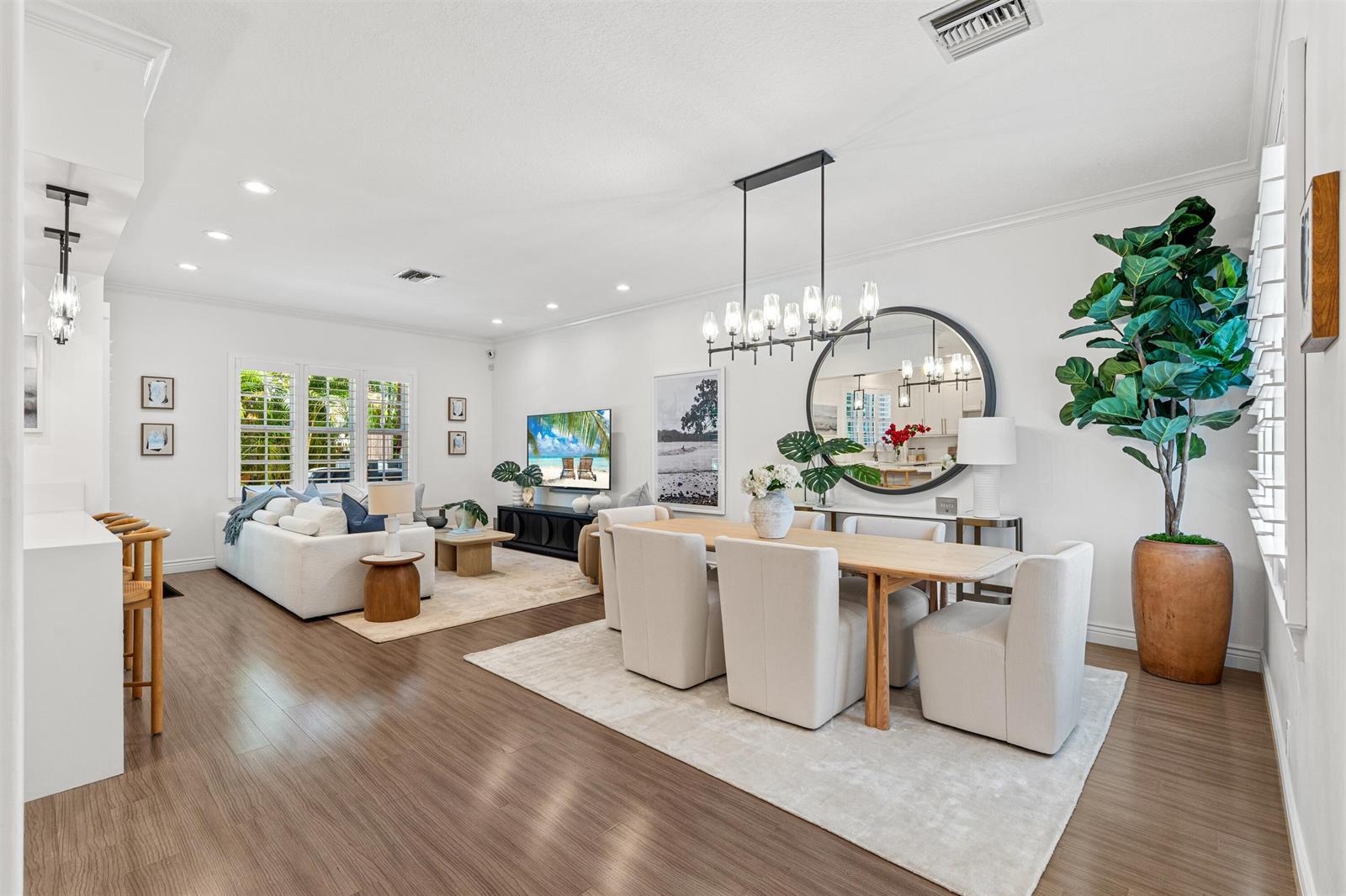 An open-concept living and dining area features white walls, wood-look flooring, and modern furniture — 1027 Coralina Lane, Delray Beach FL 33483, DELRAY BEACH, FL