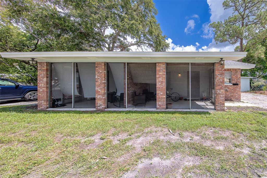 A brick-walled screened-in porch with a flat roof overlooks a grassy backyard — 153 NEW YORK AVENUE, DUNEDIN, FL