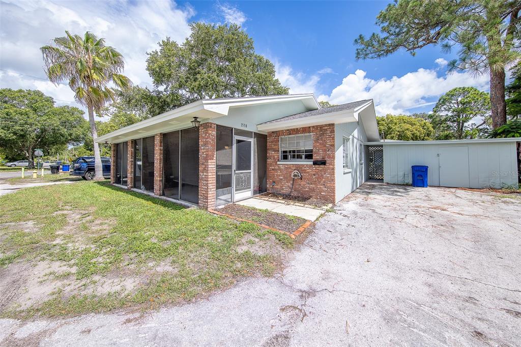 A single-story house with a brick facade, a screened-in front porch, and a paved driveway — 153 NEW YORK AVENUE, DUNEDIN, FL