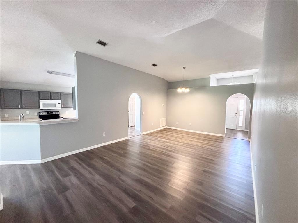 A living area with gray walls, wood-look flooring, and arched doorways leading to other rooms — 15937 WILKINSON DRIVE, CLERMONT, FL