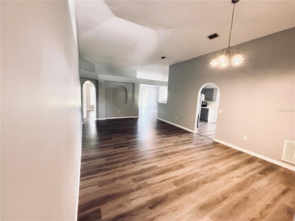 An open-concept living and dining area features vaulted ceilings, arched doorways, and wood-look flooring — 15937 WILKINSON DRIVE, CLERMONT, FL