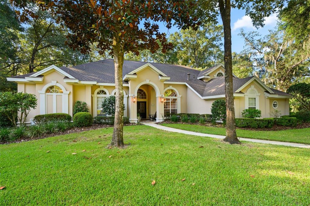 A single-story tan house with a gabled roof, arched windows, and a landscaped front yard — 4239 SW 104TH TERRACE, GAINESVILLE, FL