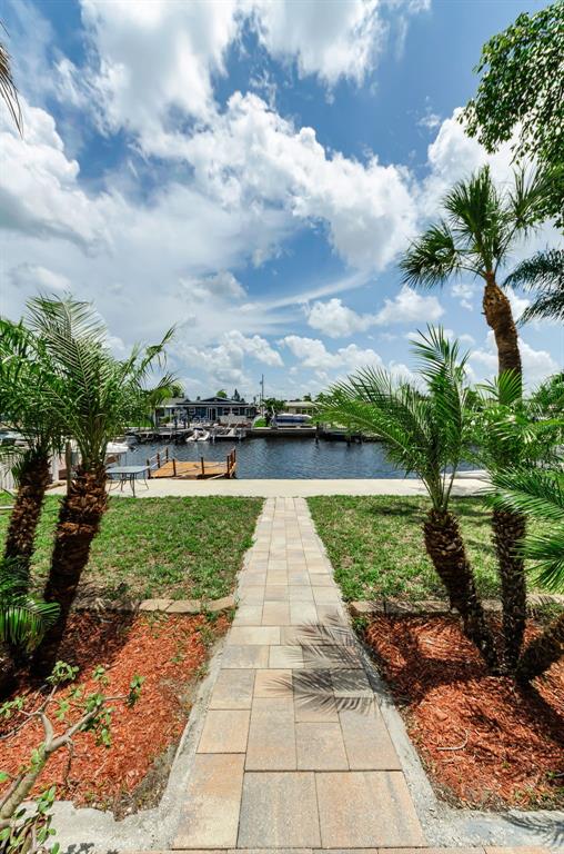 A stone walkway leads through a grassy yard toward a canal with boat docks — 4946 BLUE HERON DRIVE, NEW PORT RICHEY, FL