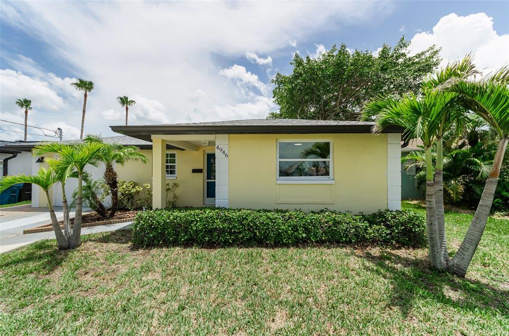 A yellow single-story house features a front porch, a hedge, and several palm trees — 4946 BLUE HERON DRIVE, NEW PORT RICHEY, FL