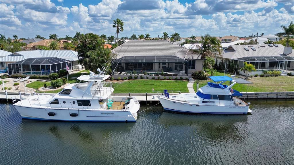 An aerial view shows two motor yachts docked in a canal behind a residential house — 1518 KINGLET DRIVE, PUNTA GORDA, FL