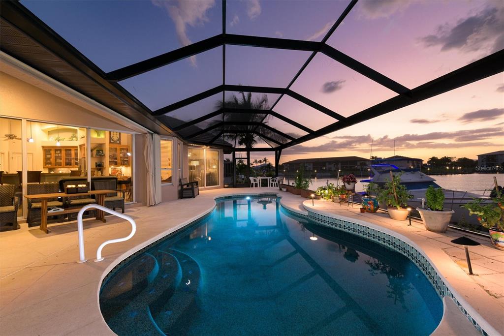 A screened-in pool patio overlooks a canal with a boat at sunset — 1518 KINGLET DRIVE, PUNTA GORDA, FL