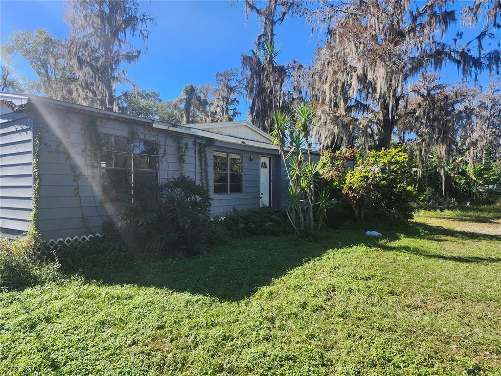 A single-story house with gray siding sits on a grassy lot with mature trees — 14328 CHISHOLM LANE, ODESSA, FL