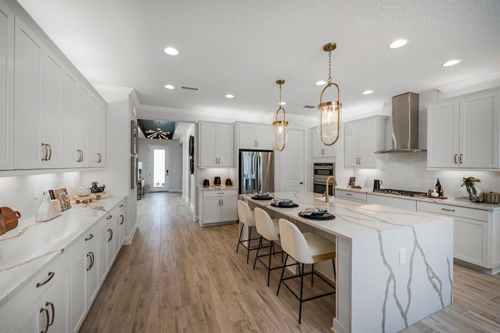 A modern kitchen features white cabinetry, a large marble island, and light wood-look flooring — 13691 LOREDO WAY, PUNTA GORDA, FL