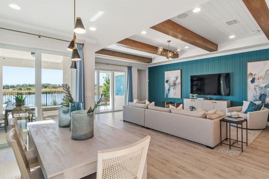An open-concept living and dining area features wood ceiling beams, a teal accent wall, and patio views — 13691 LOREDO WAY, PUNTA GORDA, FL