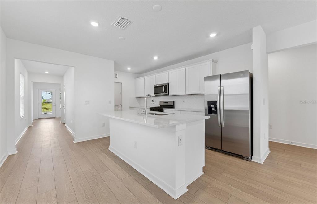 A modern kitchen features white cabinetry, stainless steel appliances, a center island, and light flooring — 6287 BROAD FIELD AVENUE, APOLLO BEACH, FL