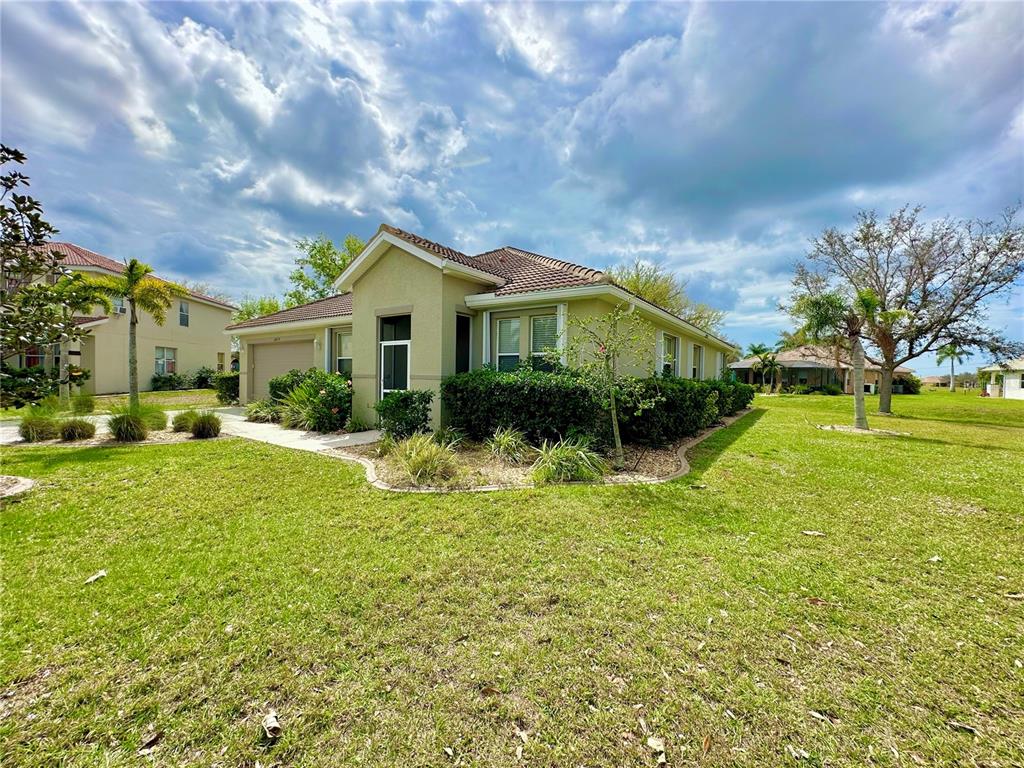 A single-story tan stucco house with a tiled roof sits on a grassy lot — 24479 VIENISON LN, PUNTA GORDA, FL